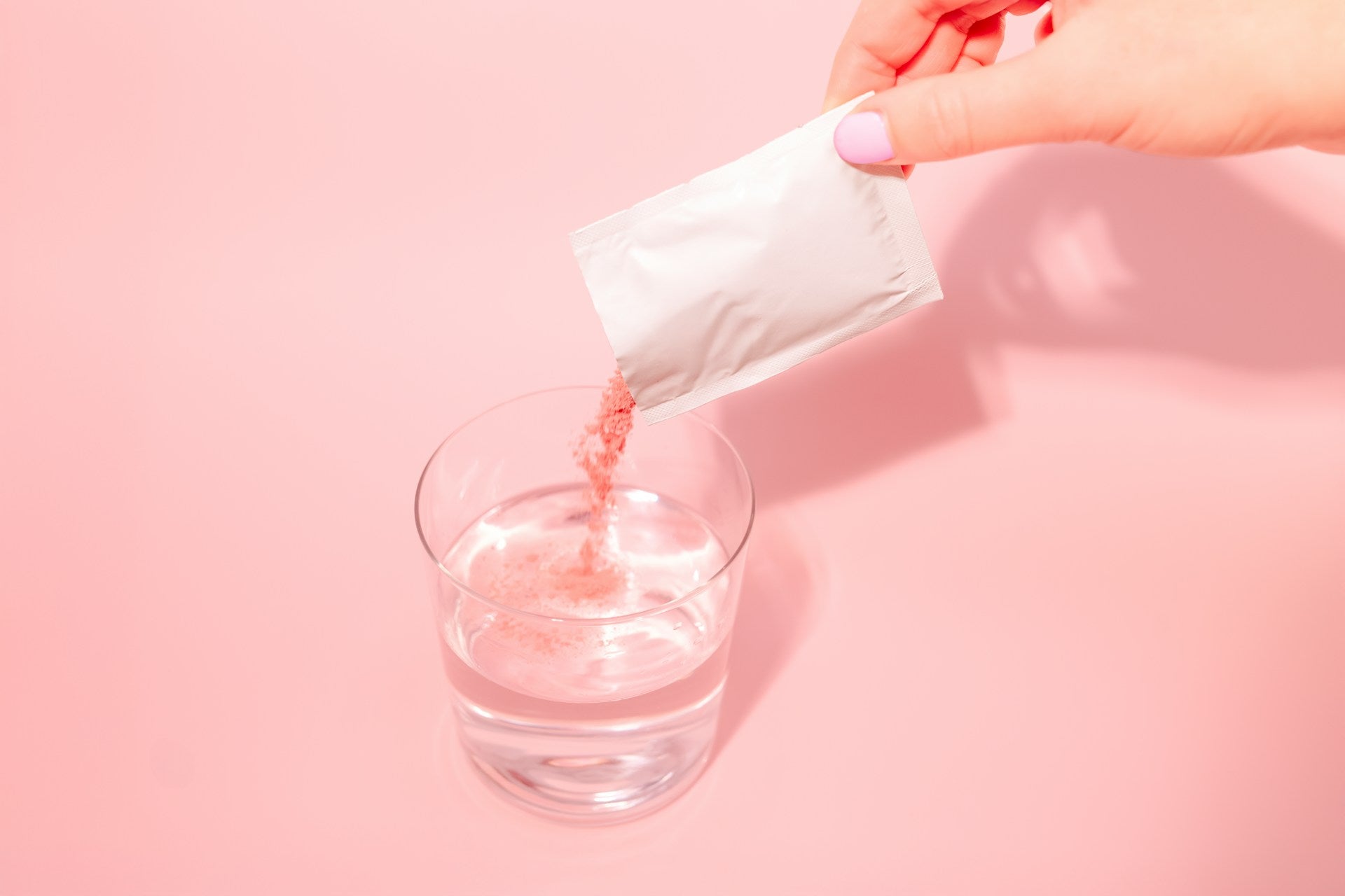 Hand pouring pink powder from an unlabelled sachet into a glass of water