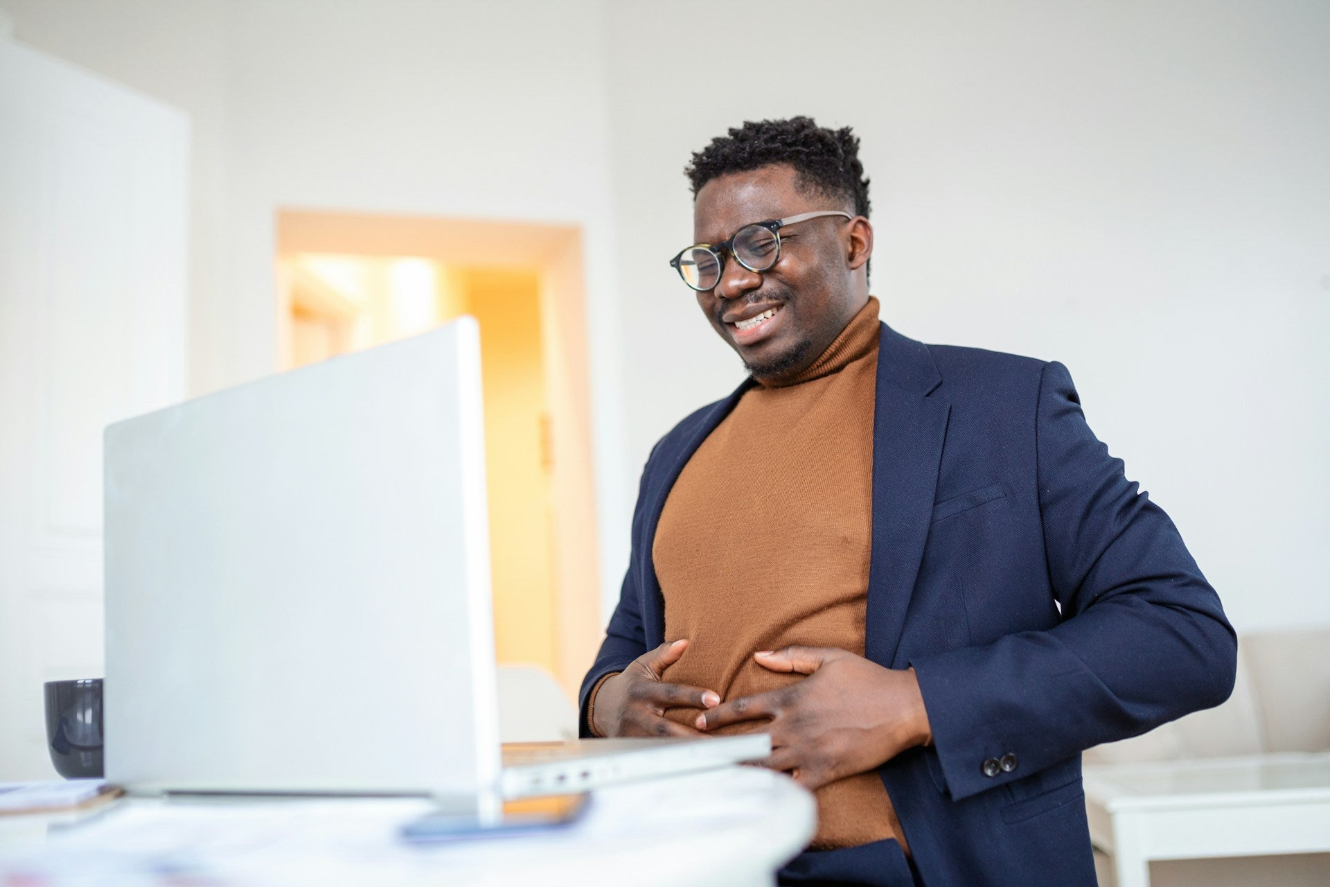Man seated at a laptop holding his abdomen with a strained expression