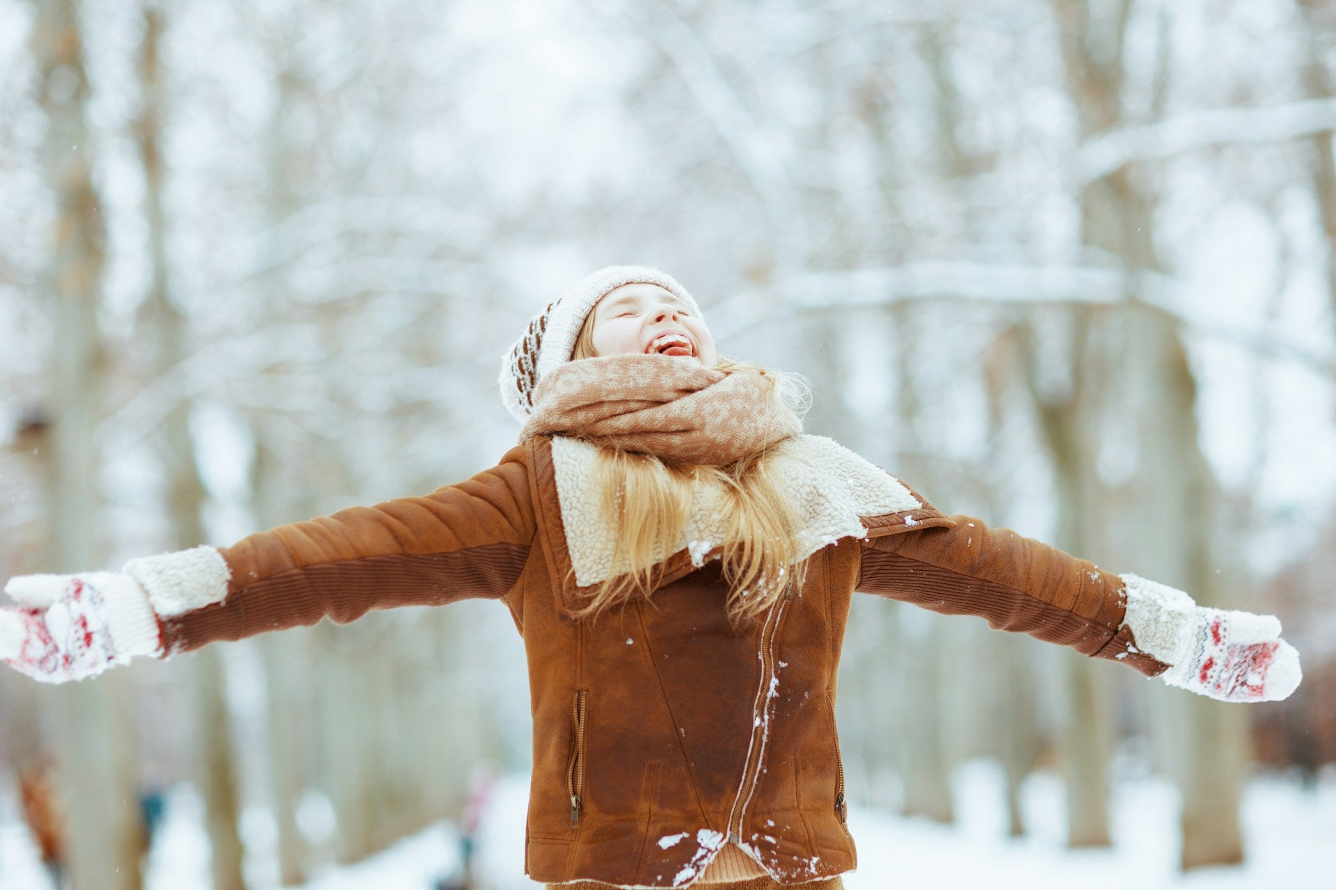 Woman in a winter coat and knitted hat holding her arms out in a snowy woodland