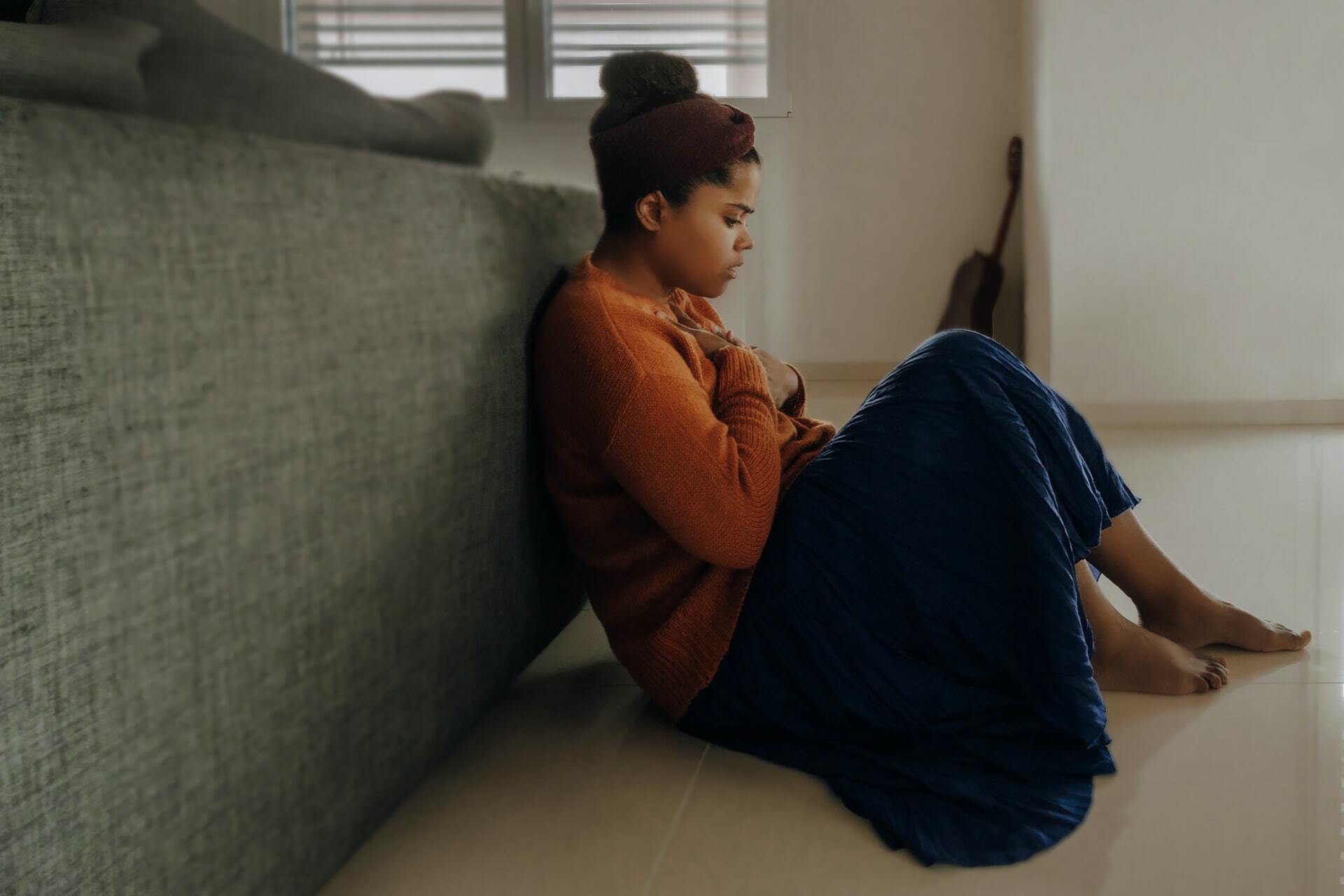 woman sitting on bedroom floor holding her chest