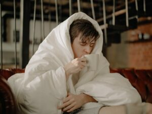 man drinking tea with blanket over him